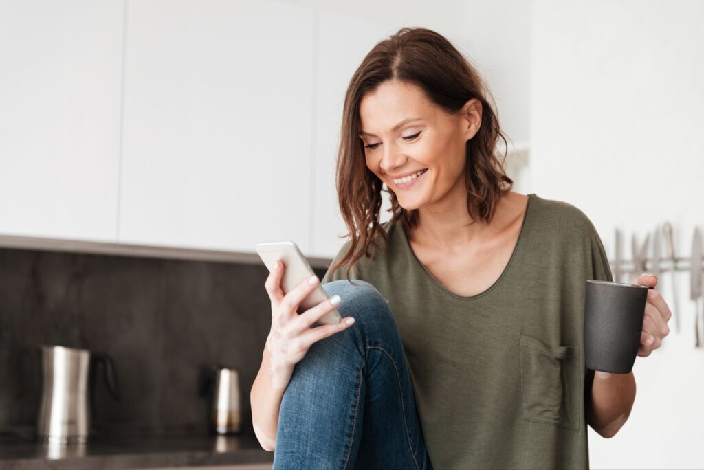 Woman using smartphone and drinking coffee in home