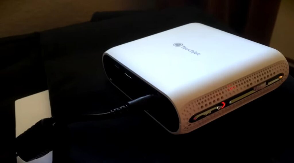 A portable projector connected to a power cable on a dark surface